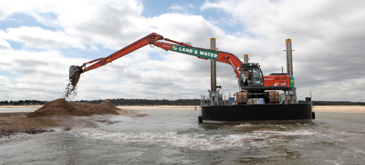 Long-reach excavator mounted on a spud barge performing mechanical dredging in shallow water