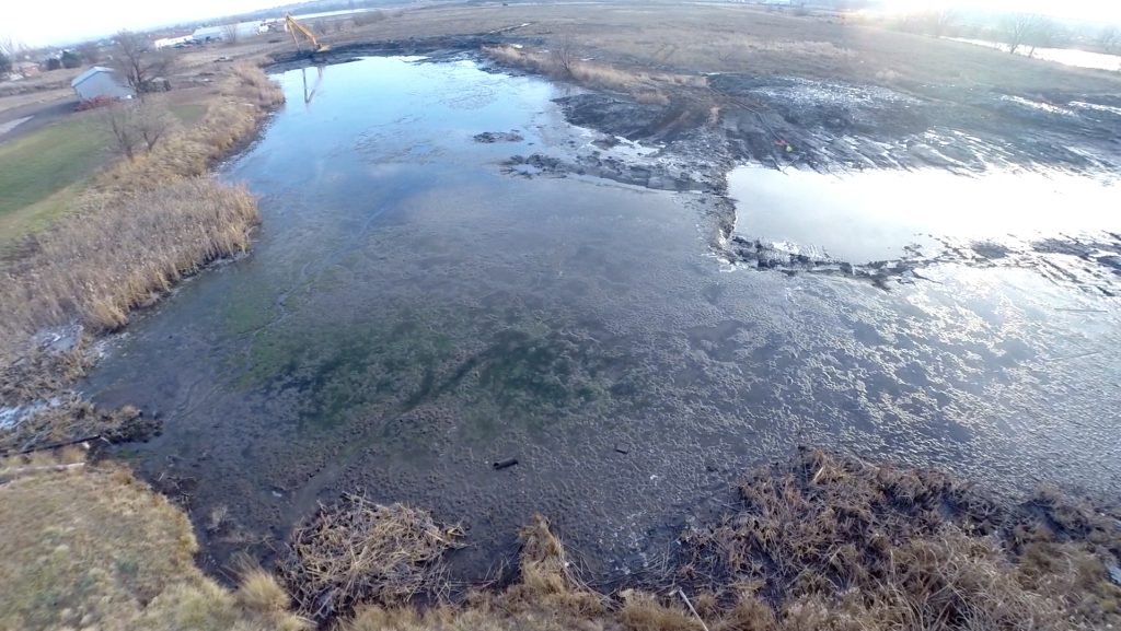 Aerial view of a small excavator dredging silt from the shoreline of a shallow lake