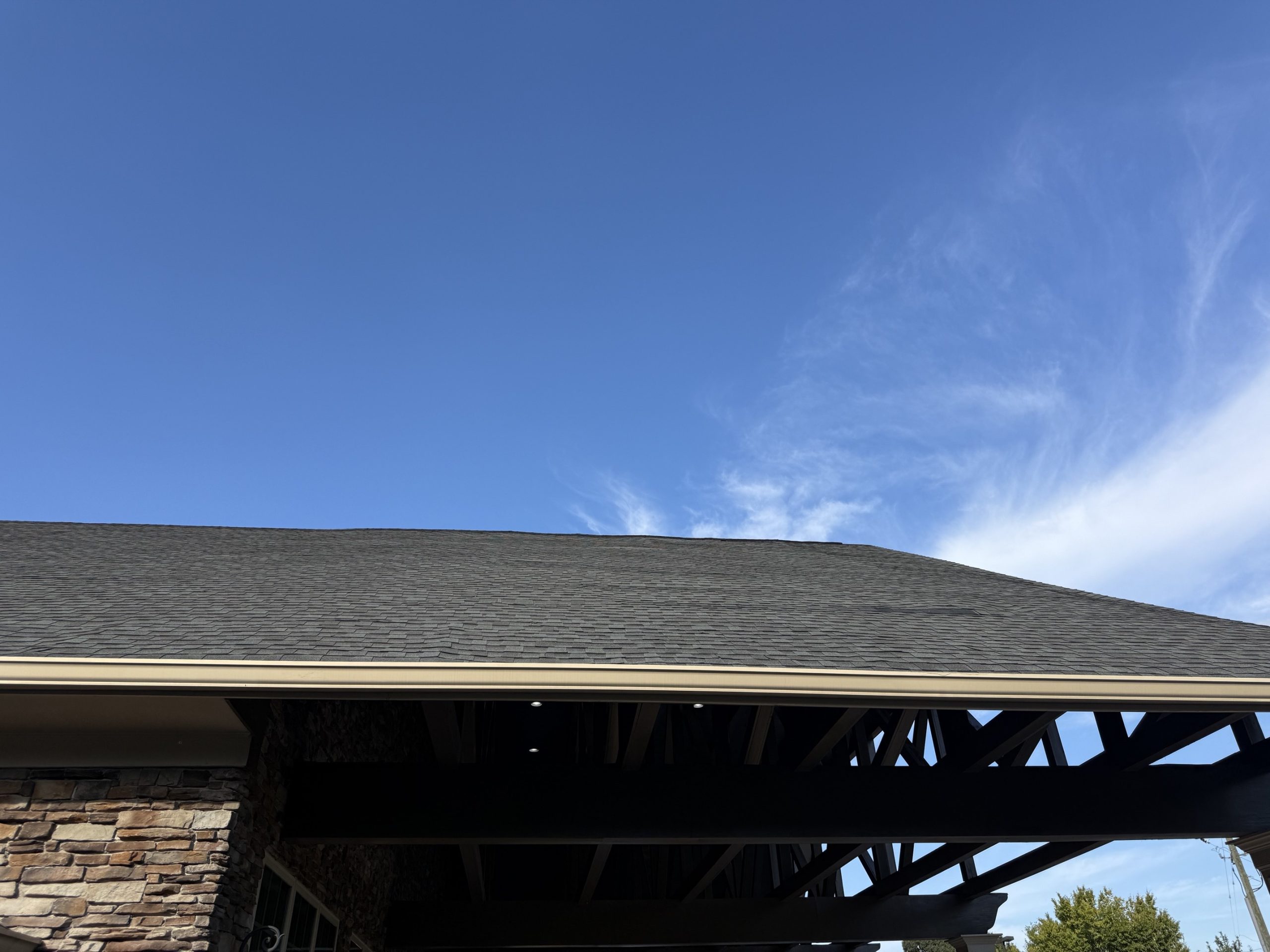 Asphalt shingle roof over a covered entry showing visible waves in the surface where sheathing clips were omitted